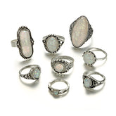 Eight-piece silver-tone opal-effect ring set arranged on a white background.