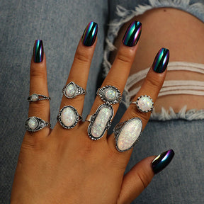 Eight-piece silver-tone opal-effect ring set worn across fingers with the pale iridescent accents visible.