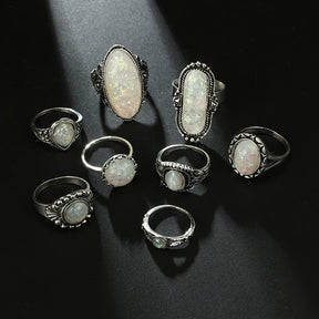 Eight-piece silver-tone opal-effect ring set arranged on black fabric.