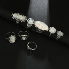 Eight-piece silver-tone opal-effect ring set displayed along a rolled black jewelry mat.