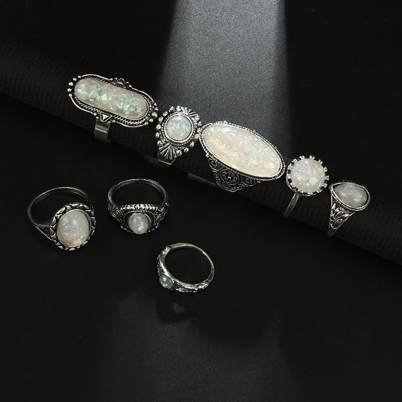 Eight-piece silver-tone opal-effect ring set displayed along a rolled black jewelry mat.