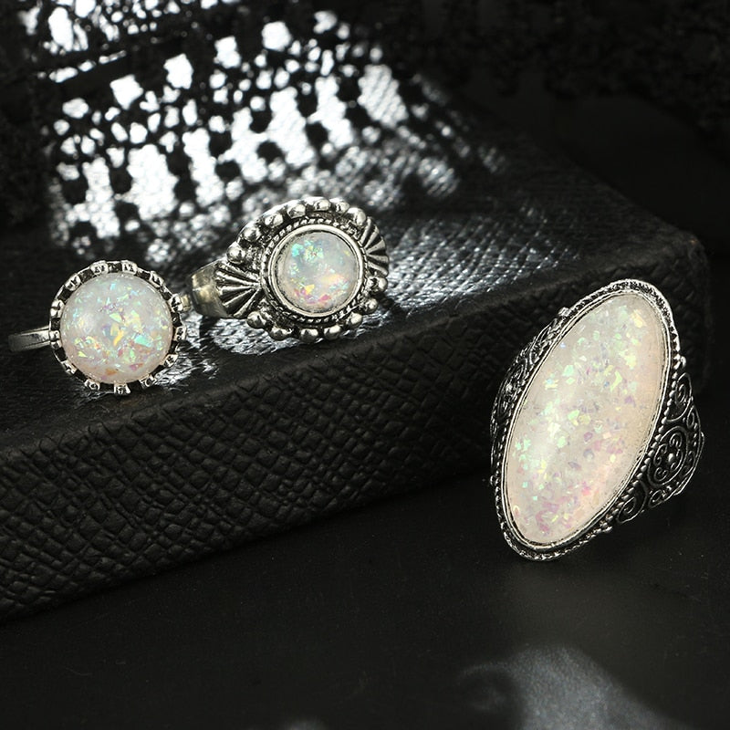Eight-piece silver-tone opal-effect ring set with a close view of three ornate settings beside black lace.