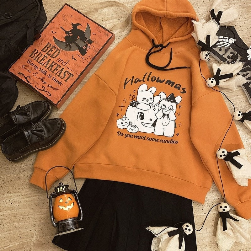 Orange Hallowmas hoodie with black drawstrings and a white rabbit-and-pumpkin graphic, laid flat with a black skirt, shoes and Halloween decorations.