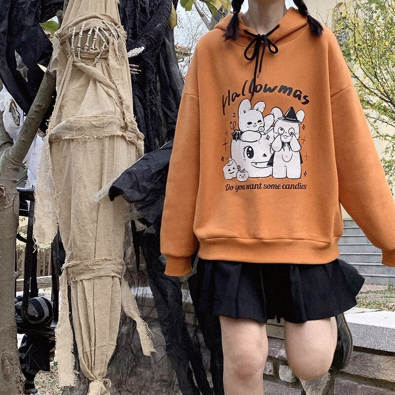 Orange Hallowmas pullover hoodie worn with a short black skirt in a decorated Halloween display, showing the relaxed shoulders and ribbed hem.