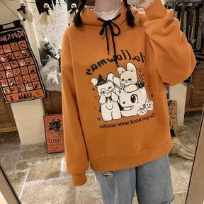 Mirror view of the orange Hallowmas hoodie with gray trousers. The black drawstrings and reflected rabbit-and-pumpkin graphic sit below the hood.