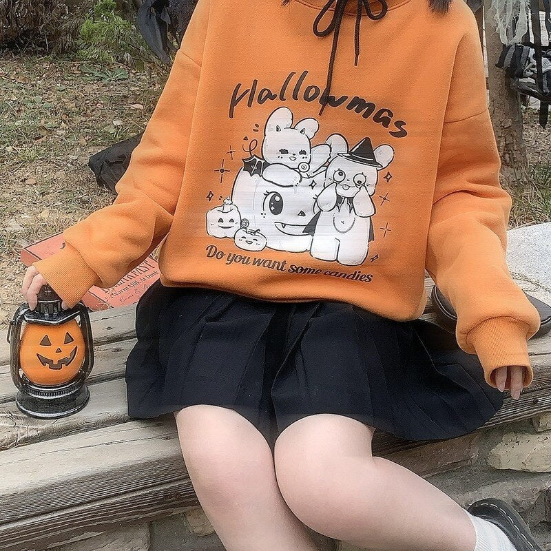 Seated model in the orange Halloween hoodie and black skirt, holding a pumpkin lantern beside the printed front and gathered sleeve cuff.
