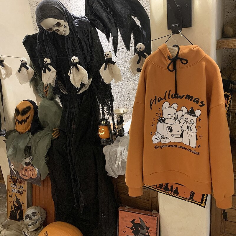 Orange Hallowmas hoodie hanging beside a tall Halloween figure, showing the full pullover shape, black drawstrings and front graphic.