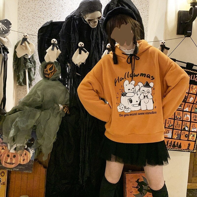 Model wearing the orange Hallowmas hoodie with hands at the waist, showing the broad sleeves and ribbed hem over a black skirt.