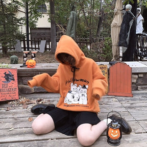 Kneeling model in the orange pumpkin-and-rabbit hoodie with the hood raised, wearing a black skirt beside a small pumpkin lantern.