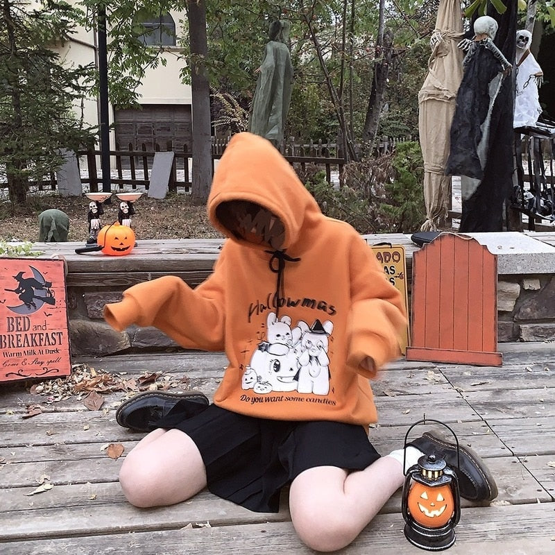 Kneeling model in the orange pumpkin-and-rabbit hoodie with the hood raised, wearing a black skirt beside a small pumpkin lantern.