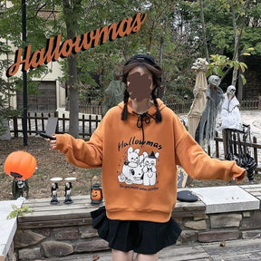 Model holding both arms outward in the orange Hallowmas hoodie, showing the roomy sleeve shape against an outdoor Halloween display.