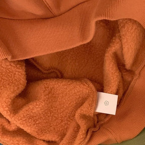 Close-up of the orange Hallowmas hoodie's soft pile interior and ribbed hem, with the fabric folded back to show both textures.