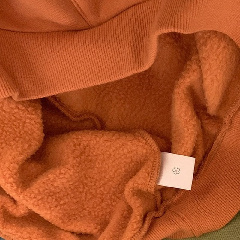 Close-up of the orange Hallowmas hoodie's soft pile interior and ribbed hem, with the fabric folded back to show both textures.