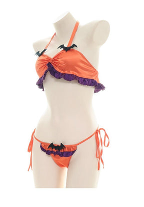 Portrait view of the orange bat lingerie set on an angled mannequin, with purple ruffles beneath the gathered top and along the front of the tie-side bottoms.