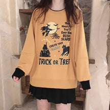 Orange Trick or Treat crewneck sweatshirt worn over a short black skirt, showing its witch, moon, castle and black cat graphic above the ribbed hem.