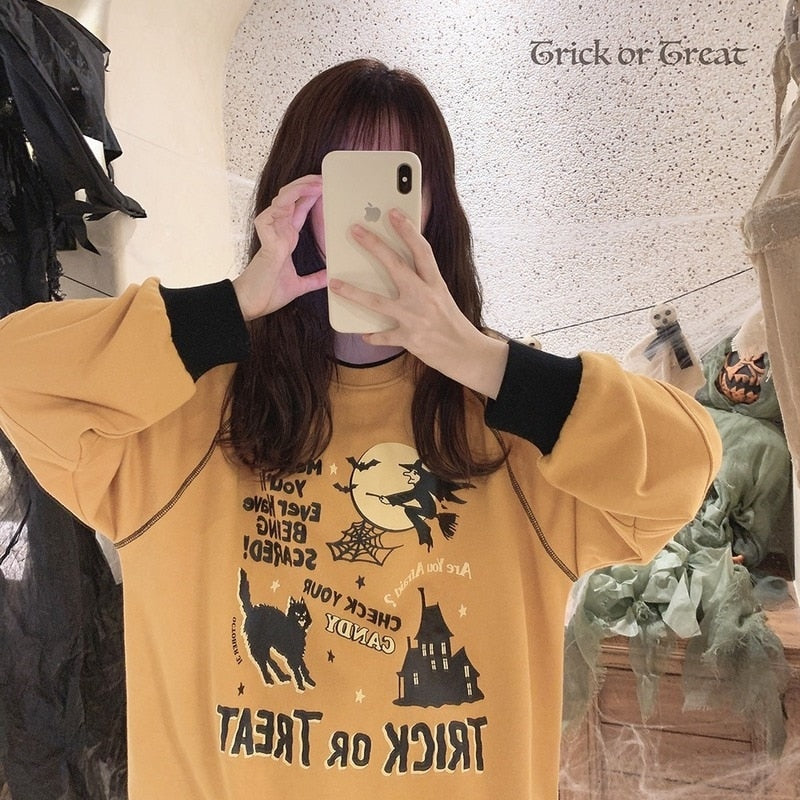 Close mirror selfie of the orange Trick or Treat sweatshirt, with a phone held at the face and the black witch graphic reflected below.