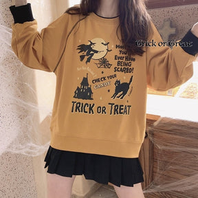 Orange Halloween sweatshirt shown with both arms raised, revealing the witch-and-moon graphic, haunted castle and ribbed lower hem.