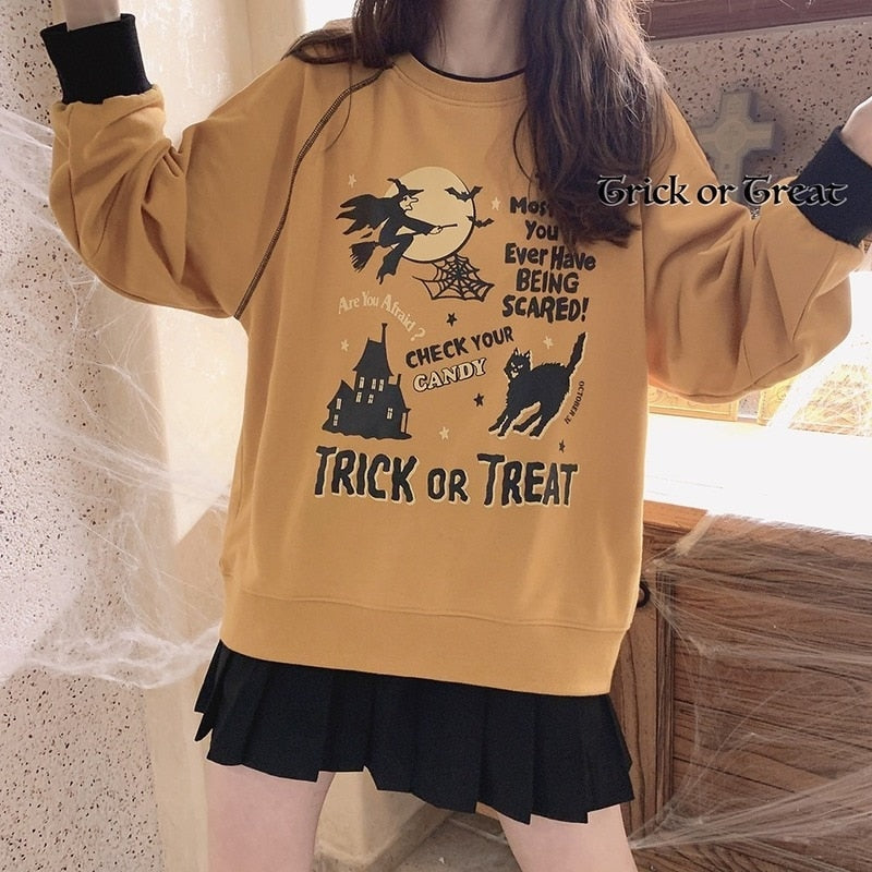 Orange Halloween sweatshirt shown with both arms raised, revealing the witch-and-moon graphic, haunted castle and ribbed lower hem.