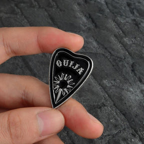 Repeated close view of the Ouija planchette pin held between fingers, showing the silver-tone sun and lettering against black enamel.