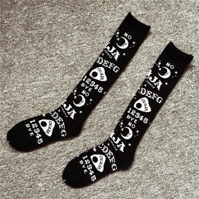 Pair of black Ouija knee socks laid flat on gray carpet, showing alphabet rows, numbers and the long spirit-board pattern.