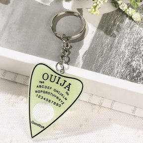 Pale green planchette keychain with a black outline and black alphabet and number details. Its circular opening reveals the white lace beneath it.