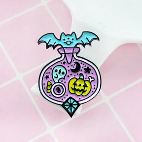 Pastel goth potion-bottle pin on a pink grid background, showing the turquoise bat above a lavender bottle filled with small Halloween motifs.