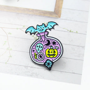 Lavender Halloween potion pin standing on a pale printed surface, with a turquoise bat, small ghost and yellow-green jack-o’-lantern outlined in black.