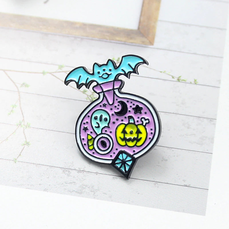 Lavender Halloween potion pin standing on a pale printed surface, with a turquoise bat, small ghost and yellow-green jack-o’-lantern outlined in black.