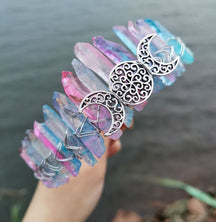 Angled view of a pastel rainbow crystal point crown with a silver-tone triple moon emblem and wire-wrapped band.