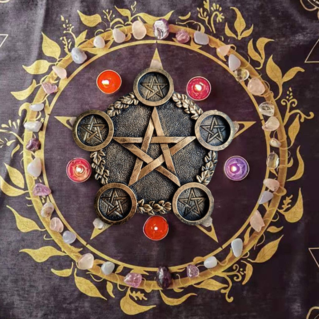Bronze-tone pentagram candle holder on a purple altar cloth with colourful small candles and stones arranged around the outside.