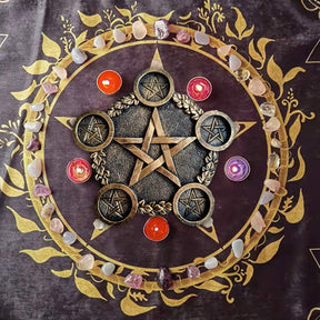 Bronze-tone pentagram candle holder on a purple altar cloth with colourful small candles and stones arranged around the outside.