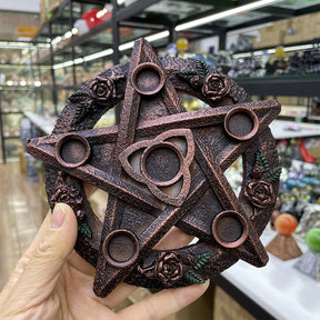A hand holds a copper-toned rose-and-triquetra candle holder, showing the depth of its raised star and five small round platforms.