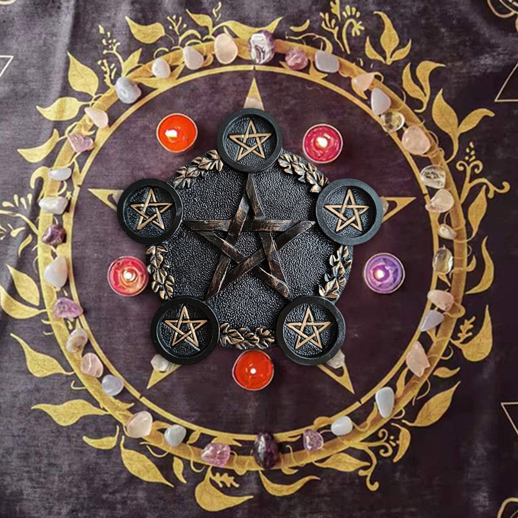 Black pentagram holder shown from above on a purple cloth, surrounded by small colourful candles and pale stones.