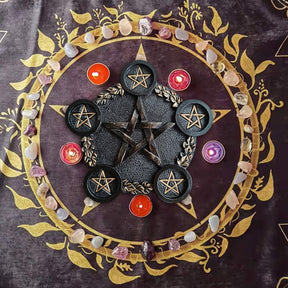 Black pentagram holder shown from above on a purple cloth, surrounded by small colourful candles and pale stones.
