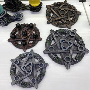 Several rose-and-triquetra candle holders in metallic-tone finishes arranged on a white display surface, including extra display variations.