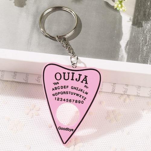 Solid pink planchette keychain with black lettering and a black border, attached to a short silver-tone chain and ring above a circular cutout.