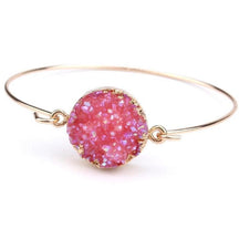 Pink round druzy quartz cuff bracelet with a textured sparkling face and slender gold-tone band on white.
