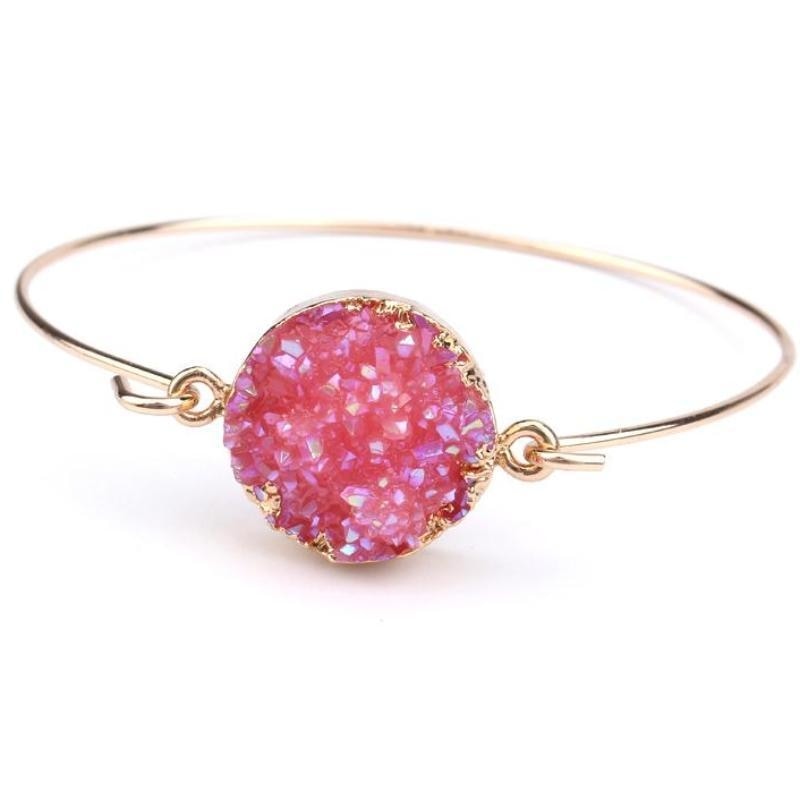 Pink round druzy quartz cuff bracelet with a textured sparkling face and slender gold-tone band on white.