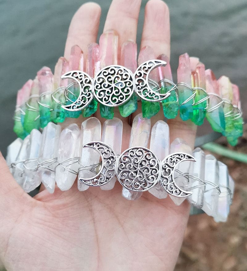 Pink-green and clear crystal crowns paired together, with their pointed stones and silver-tone triple moon emblems visible.
