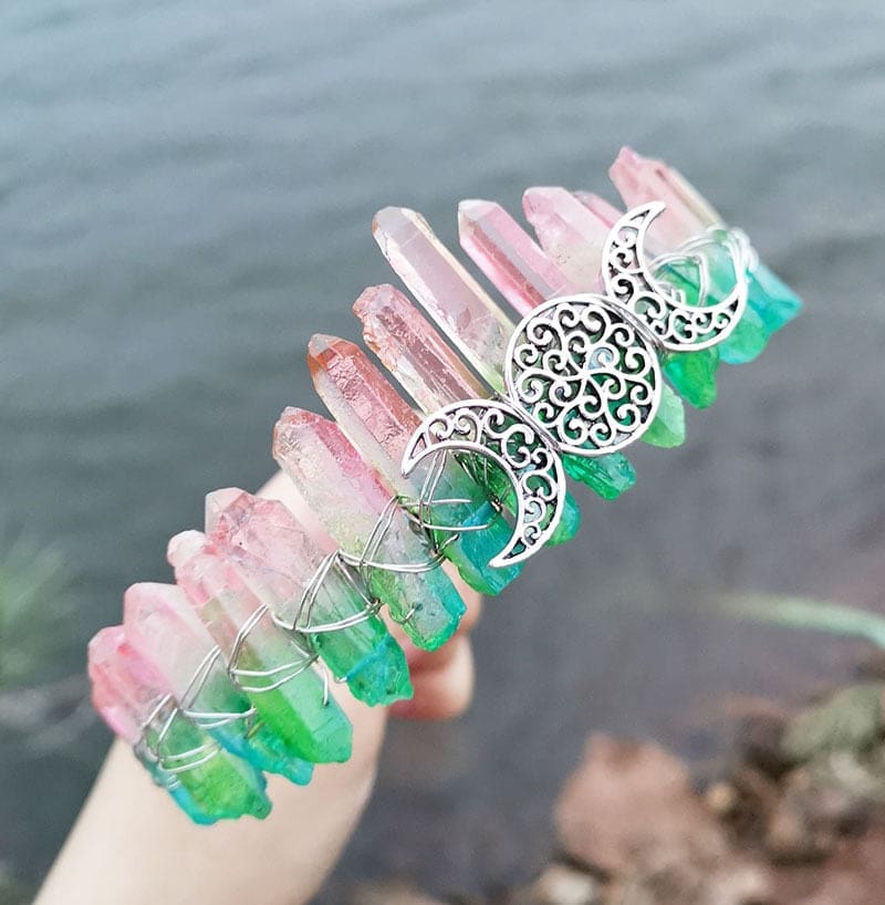 Angled view of a pink green crystal point crown with a silver-tone triple moon emblem and wire-wrapped band.