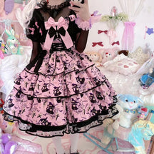 Pink tiered Halloween dress with oversized bows, black front lacing and a print of pointed-hat figures, bats, crosses and spiderwebs, worn over a sheer black blouse.