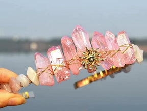 Pink crystal tiara with a gold-tone sun face and pale points forming an uneven crown around the emblem.