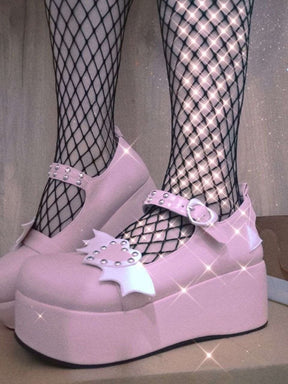 Pink winged-heart platform Mary Janes worn with black fishnet tights, showing the white wings, heart buckle and thick pink soles.