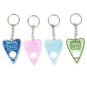 Four planchette keychains arranged in a row on white, showing dark blue glitter, translucent pink, light blue glitter and pale green designs.