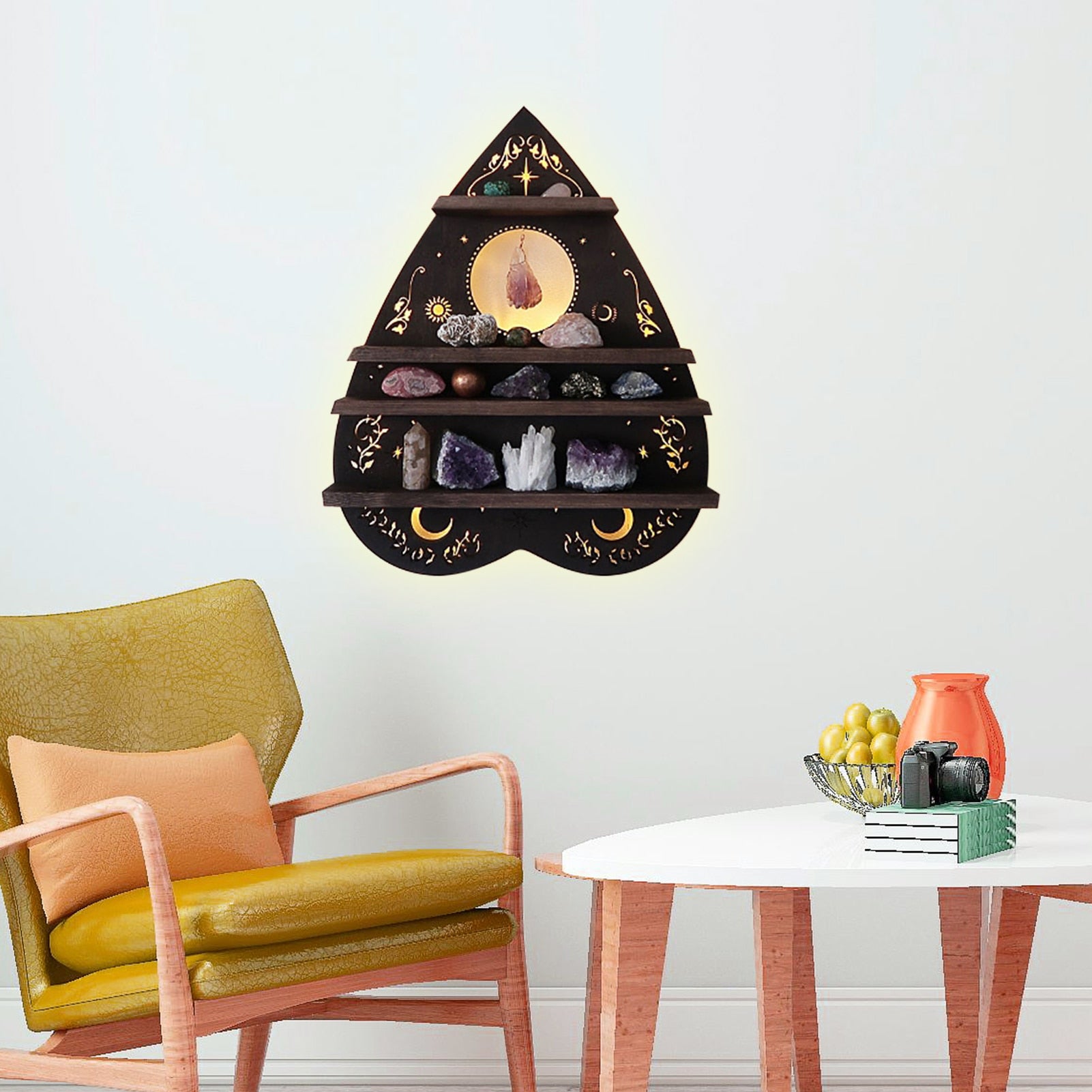 Dark planchette shelf on a pale wall above a yellow chair and a round white table, with celestial motifs and small stones across the ledges.