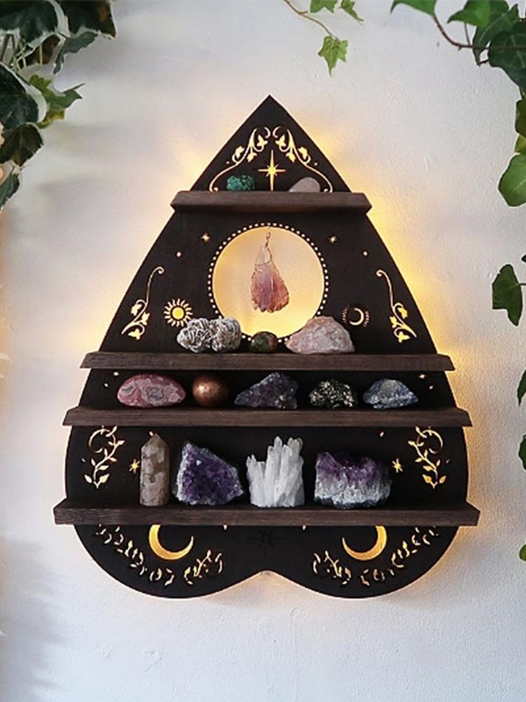 Dark brown planchette-shaped wall shelf with four display ledges, golden moons and vine motifs. Crystals are arranged across the tiers, with a pendant hanging over the circular detail near the top.
