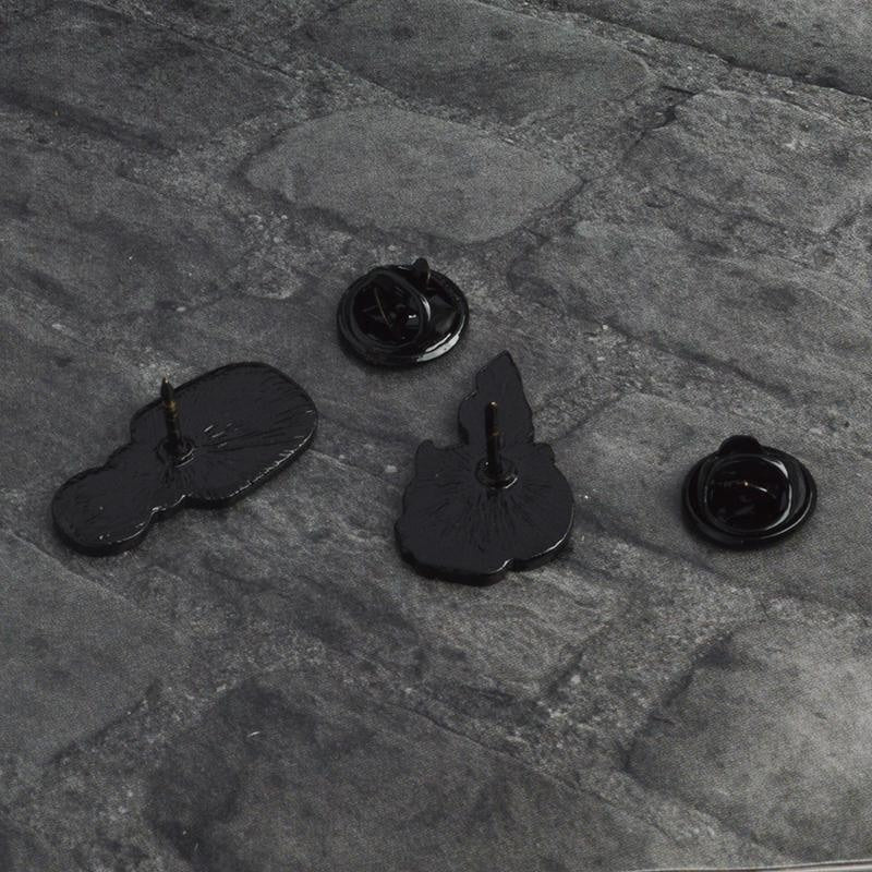 Reverse sides of the potion and skull-candle pins on gray fabric, with their single posts and separate black butterfly-clutch backs.