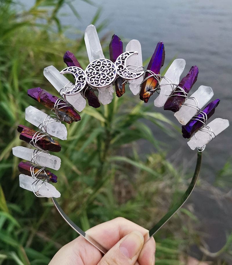 Purple-clear crystal crown against a green outdoor background, with a silver-tone triple moon emblem centred beneath the points.