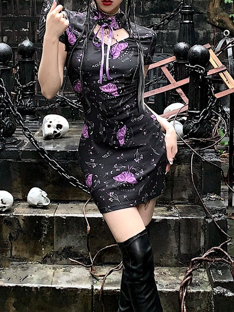 Front of the black and purple moth mini dress, with one hand at the hip. A long purple ribbon falls below the keyhole collar against the patterned chest.