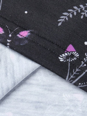 Close view of the stitched mini-dress hem on black fabric printed with purple flowers and tiny mushroom shapes.